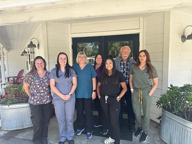 The Healdsburg Veterinary Hospital Team, a group of seven staff members, stands outside the clinic, smiling at the camera, with some wearing scrubs and others in casual attire.